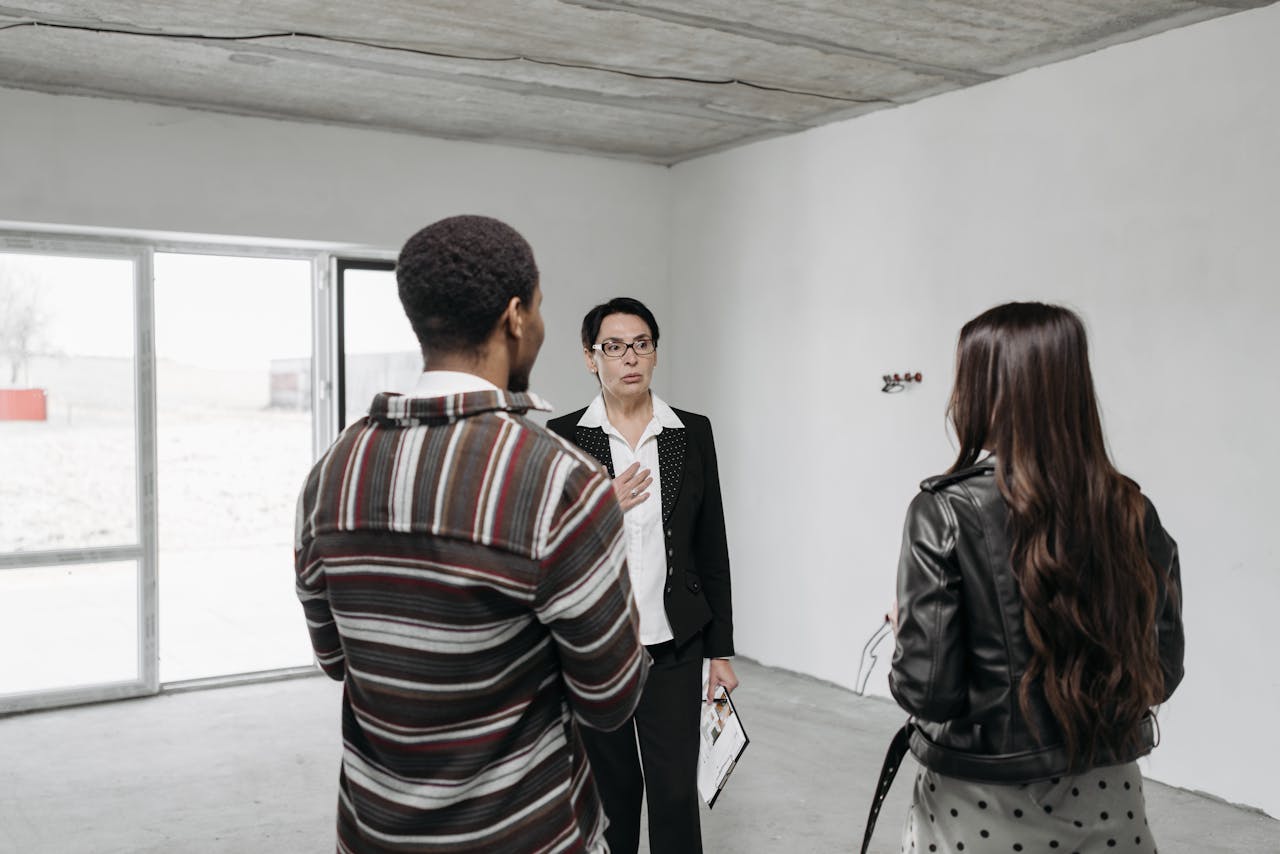 Realtor showing young couple a house, discussing details inside a modern, unfurnished space.